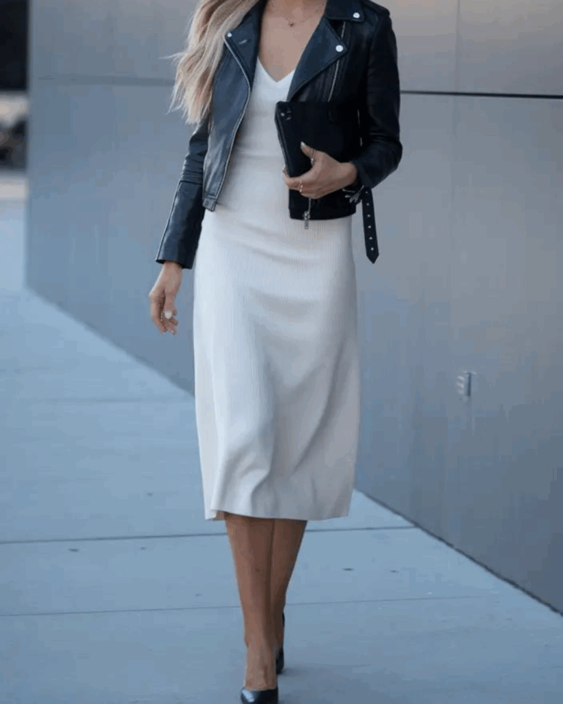 A woman wears a sleek white midi dress with a cropped black leather jacket, paired with heels and a small clutch.