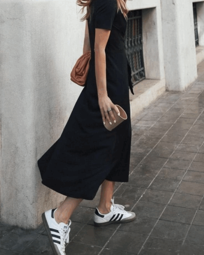 A woman styles a casual midi dress with clean white sneakers and a crossbody bag, blending comfort and chic style.