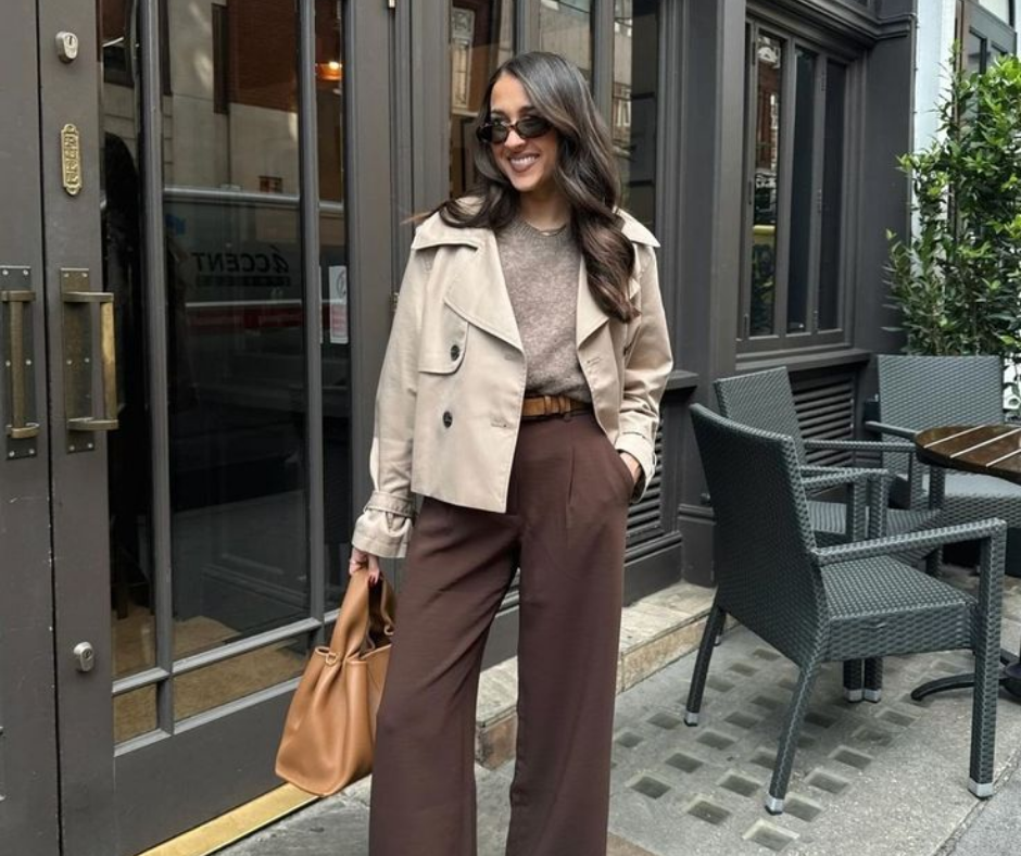 Stylish woman wearing a beige cropped trench coat, taupe sweater, and high-waisted brown wide-leg trousers, standing confidently outside a cafe.
