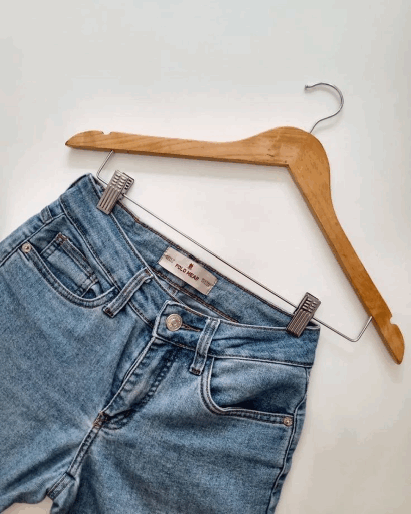 Light blue denim jeans hanging on a wooden hanger with metal clips against a white background.