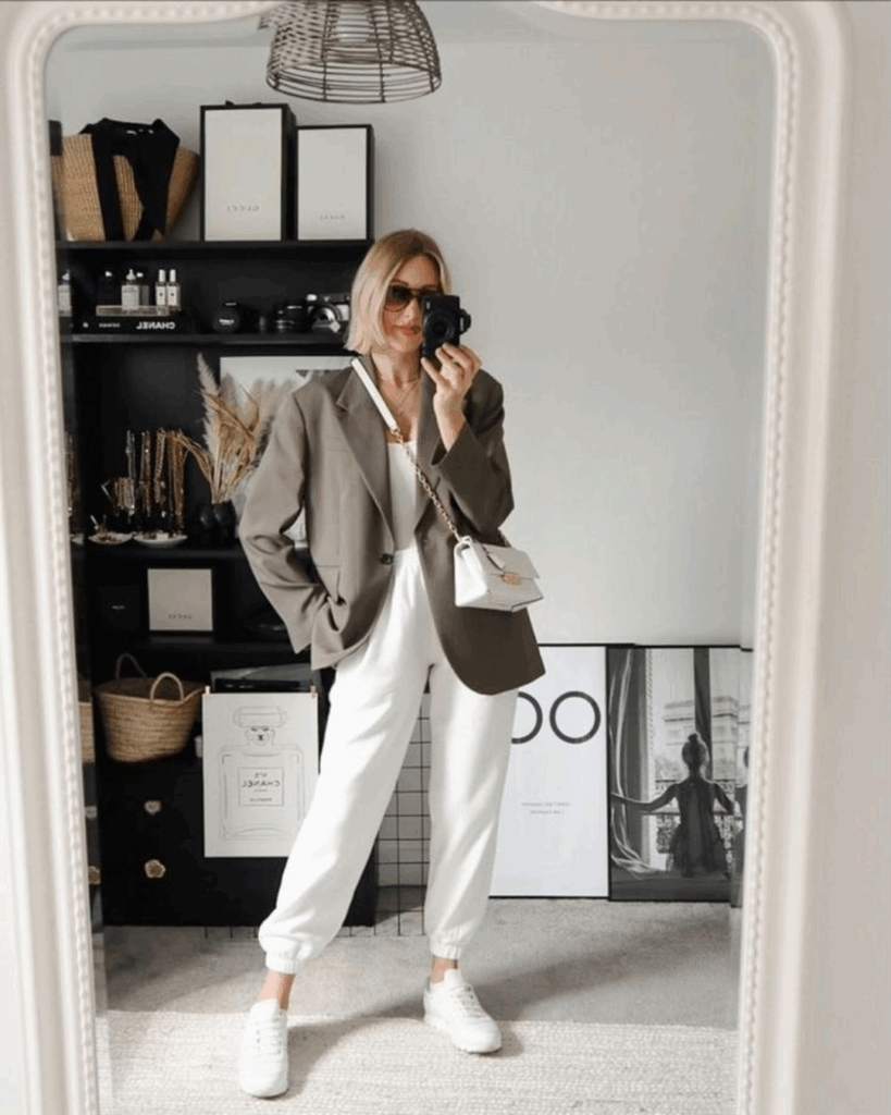 Woman taking a mirror selfie in a chic outfit featuring a taupe oversized blazer, white joggers, white sneakers, and a mini crossbody bag.
