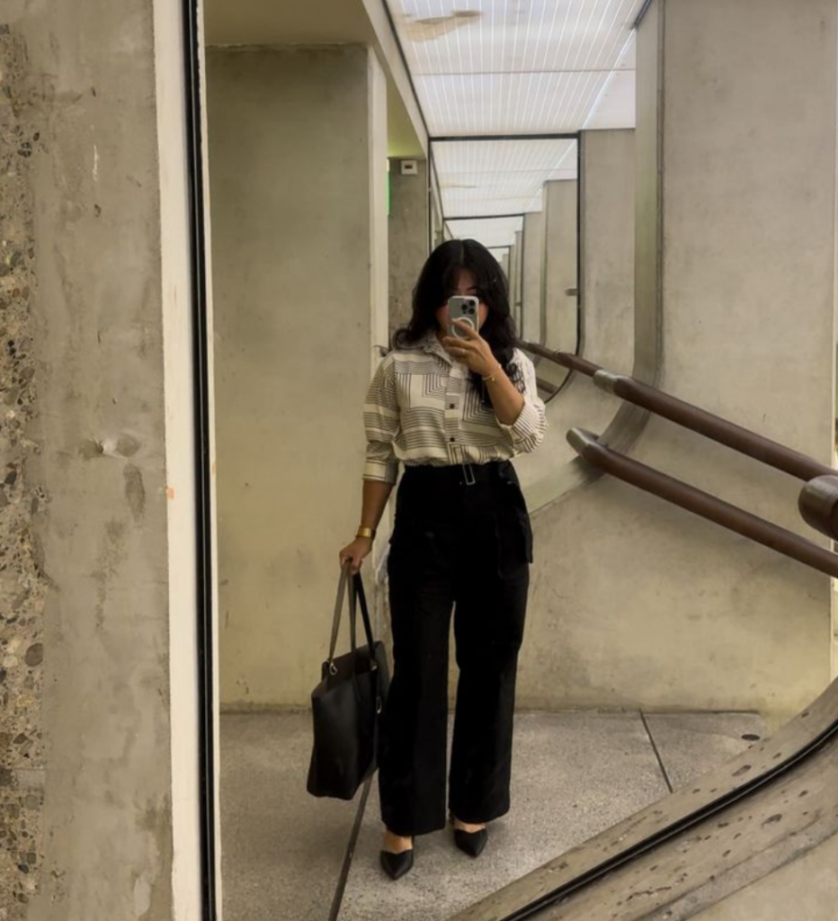 Woman wearing black trousers and a neutral top with a structured bag while walking indoors